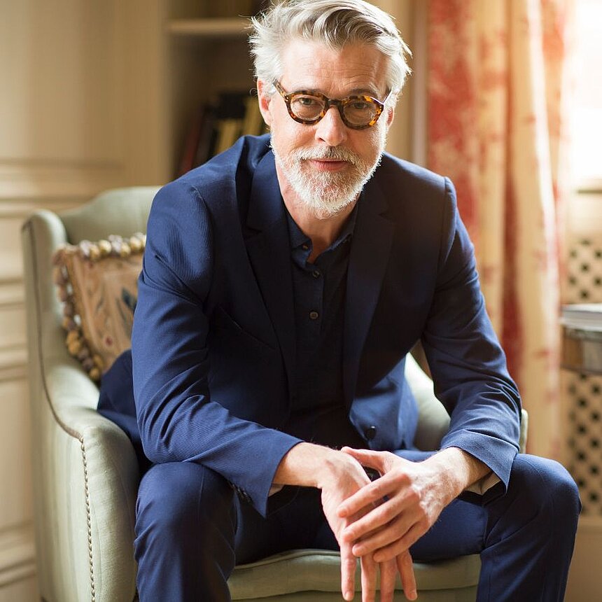 Smarte Investments in die Zukunft der Hotellerie Erfahrener Geschäftsmann in stilvollem Anzug sitzt entspannt in einer eleganten Hotellounge und blickt zuversichtlich