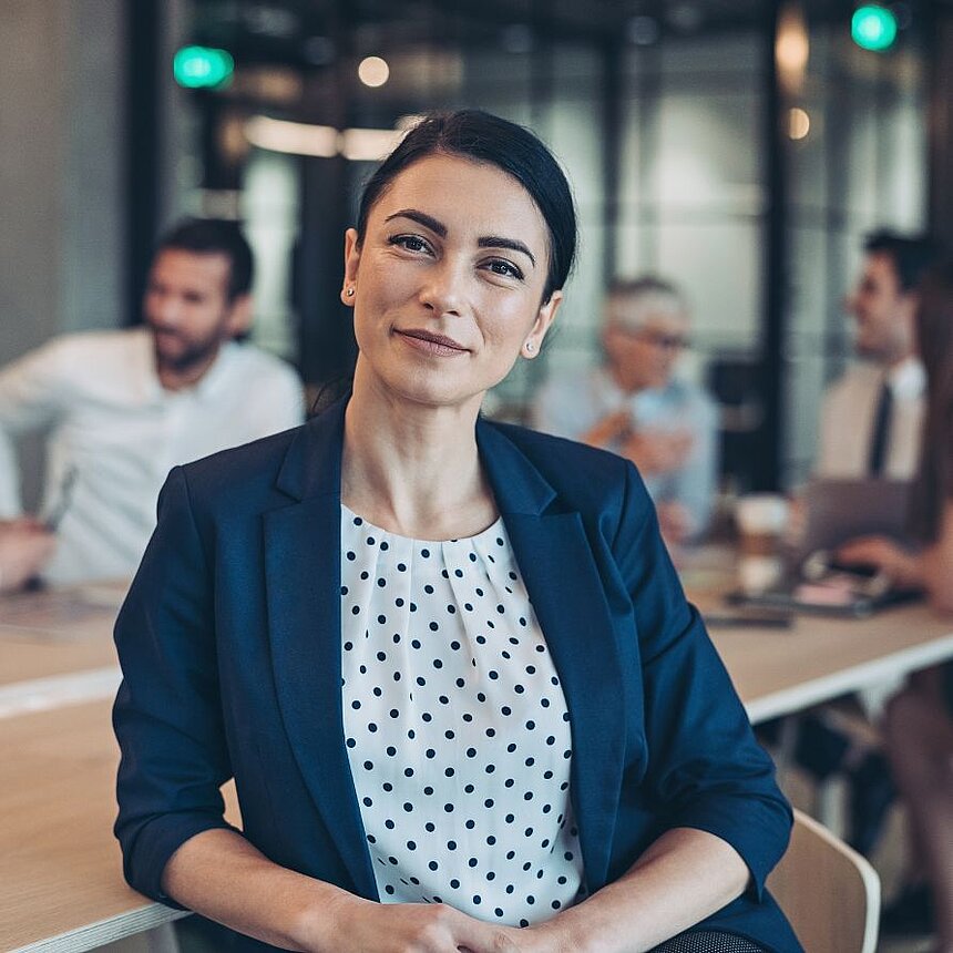 Erfolg mit Weitblick – Investieren in die Zukunft der Hotellerie Selbstbewusste Geschäftsfrau in elegantem Business-Outfit sitzt in moderner Meeting-Umgebung und blickt vorausschauend